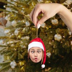 a woman holding a christmas ornament in front of a tree