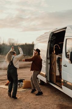 two people standing in front of a van with the door open and one person reaching for something