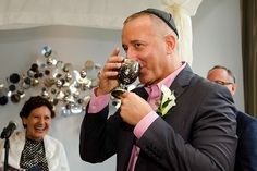 a man drinking from a wine glass in front of a group of people at a wedding