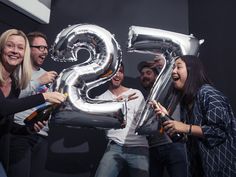 a group of people standing around each other holding up large silver balloons in the shape of the number twenty