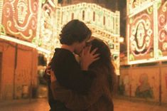 a man and woman kissing in front of an elaborately decorated building with lights on it