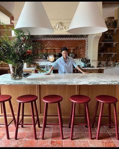 a man behind the bar in a restaurant with four stools and two lamps above it