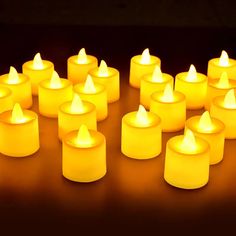 many lit candles are arranged in rows on a dark surface with one glowing yellow candle