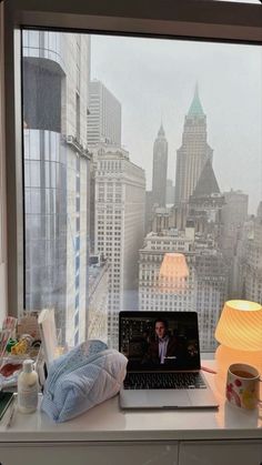 an open laptop computer sitting on top of a desk next to a window with cityscape in the background