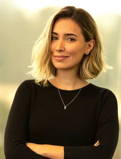 a woman with blonde hair wearing a black shirt and green necklace smiling at the camera