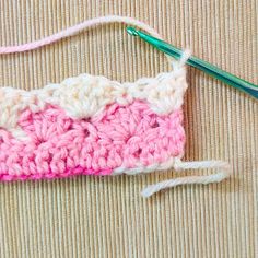 a crocheted pink and white object next to a knitting needle on a beige surface