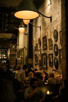 people sitting at tables in a restaurant with pictures on the wall and lights hanging from the ceiling