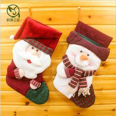 two christmas stockings with santa and snowman decorations hanging from hooks on a wooden wall