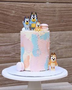 a pink and blue frosted cake with small figurines sitting on top of it