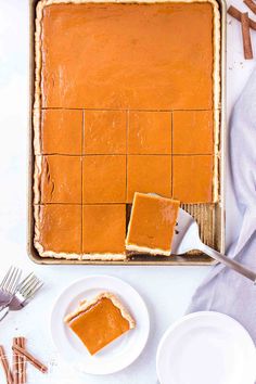 two slices of pumpkin pie sitting on top of a pan next to plates and forks