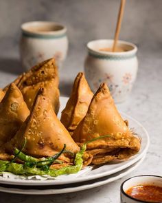 some food is on a white plate with sauces and two cups in the background