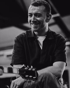 a black and white photo of a man smiling with a guitar in his hand,