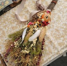 an arrangement of dried flowers and feathers is on a table with ribbon tied around it