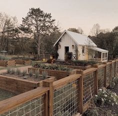 a fenced in garden area with several wooden planters and a small white house