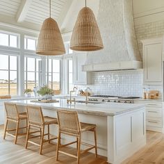 a large kitchen with white cabinets and wooden chairs in front of an island that has two pendant lights hanging from the ceiling