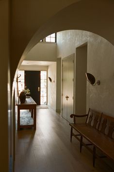 an arched hallway leading to a living room and dining area with wooden benches on either side