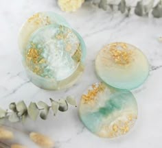 three soaps sitting on top of a marble counter next to flowers and leaves with gold flecks