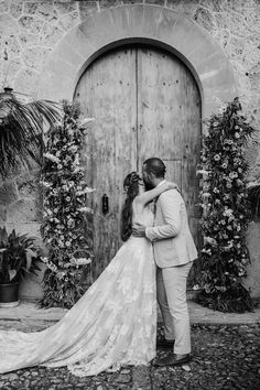 a bride and groom kissing in front of an old wooden door with flowers on it