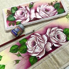 two pink roses painted on canvases next to a brush