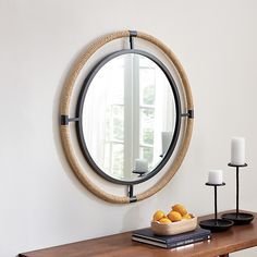 a round mirror hanging on the wall above a wooden table with candles and oranges