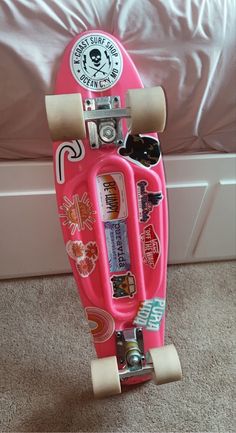 a pink skateboard with stickers on it sitting in front of a white bed