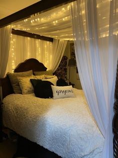 a bed with white drapes and lights on the headboard is decorated in black and white