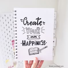 someone holding up a notebook with the words create your own happiness written on it in front of them