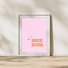 a pink poster with the words nice bum in gold foil on it next to a wooden floor