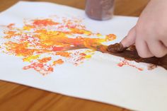 a child is painting with orange and yellow colors on paper while holding a brush in his hand