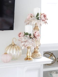 a white mantle with candles, flowers and other decorative items on it in front of a flat screen tv