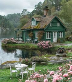 a green house sitting on top of a lush green field next to a lake with pink flowers