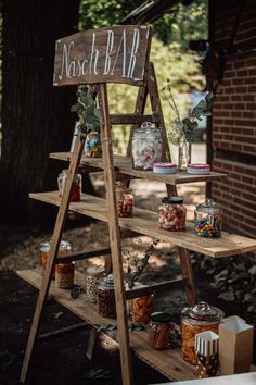 a wooden shelf with jars and candy on it in front of a brick building under a tree