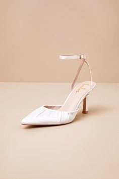 a pair of white high heeled shoes on a beige background, with one shoe in the foreground