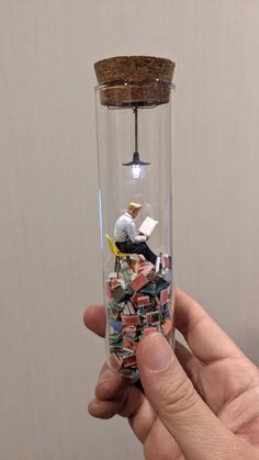 a hand holding a glass tube filled with lots of small objects and a light bulb hanging from the ceiling