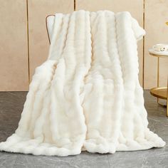 a large white fur blanket sitting on top of a floor next to a chair and table