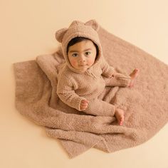 a baby in a teddy bear outfit laying on a blanket and looking at the camera