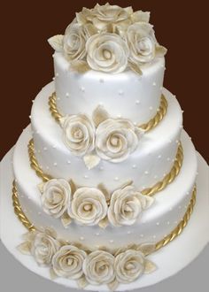 a three tiered wedding cake with white roses on top and gold trimmings