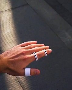 a person's hand with two white rings on it, and the other one is holding something in their left hand