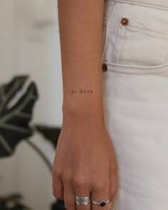 a woman's wrist with the word be here tattooed on it, in black ink