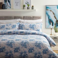 a bed with blue flowers on it in a bedroom next to a nightstand and painting