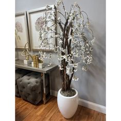 a white vase filled with flowers on top of a wooden floor next to a wall