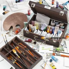 an open wooden box filled with lots of paint and brushes on top of a table