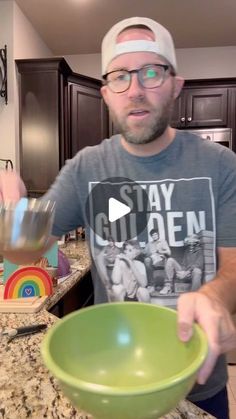 a man holding a green bowl in his hand while standing next to a kitchen counter