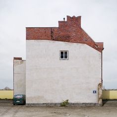 a car parked in front of a white building with a red roof and brick chimney