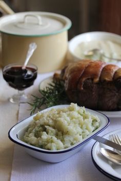 a table topped with white plates and bowls filled with meat, potatoes and gravy