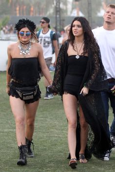 two women in black outfits walking on the grass with one woman wearing an open - back dress