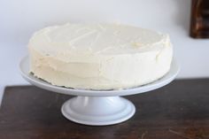 a white frosted cake sitting on top of a wooden table next to a bottle