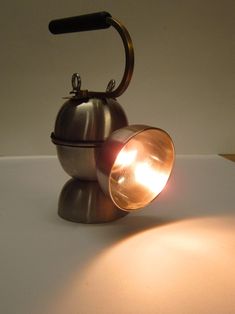 an old fashioned tea kettle sitting on top of a white table with a light coming from it