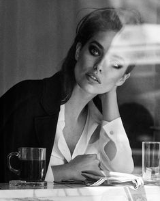 a black and white photo of a woman sitting at a table with two cups in front of her