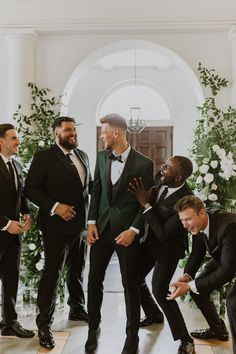 four men in tuxedos are laughing and posing for the camera while another man looks on